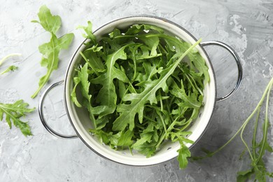 Photo of Fresh green arugula leaves in colander on grey textured table, top view