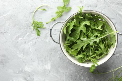 Photo of Fresh green arugula leaves in colander on grey textured table, top view. Space for text