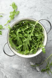 Photo of Fresh green arugula leaves in colander on grey textured table, top view