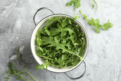 Photo of Fresh green arugula leaves in colander on grey textured table, top view