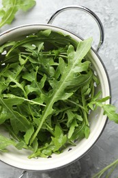 Photo of Fresh green arugula leaves in colander on grey textured table, top view