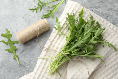 Photo of Bunch of fresh green arugula leaves and spool of thread on grey textured table, flat lay