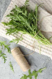 Photo of Bunch of fresh green arugula leaves and spool of thread on grey textured table, flat lay