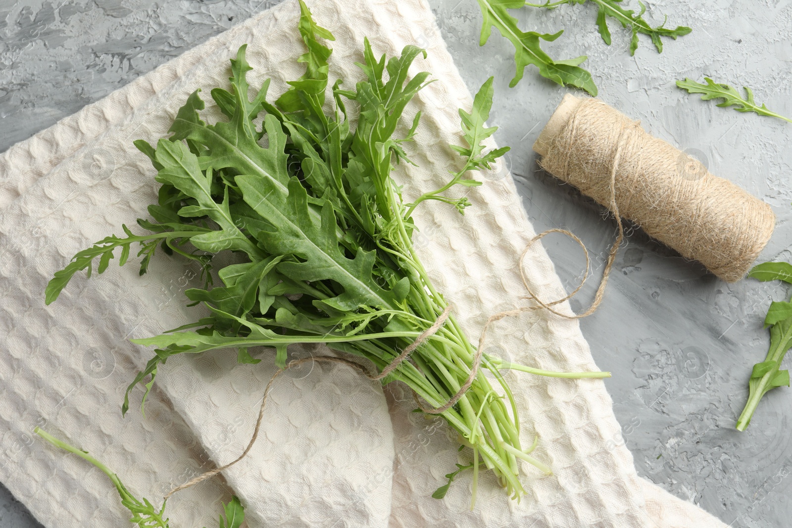 Photo of Bunch of fresh green arugula leaves and spool of thread on grey textured table, flat lay