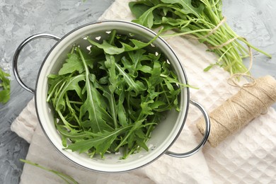 Photo of Fresh green arugula leaves in colander and spool of thread on grey table, flat lay