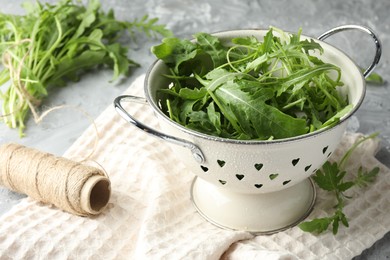 Photo of Fresh green arugula leaves in colander and spool of thread on grey table