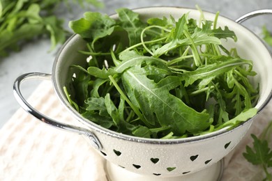 Photo of Fresh green arugula leaves in colander on table, closeup