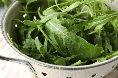 Photo of Fresh green arugula leaves in colander on table, closeup