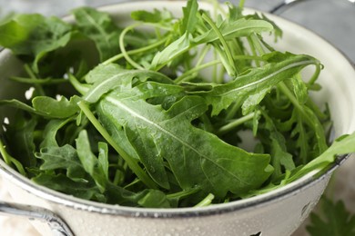 Photo of Fresh green arugula leaves in colander on table, closeup