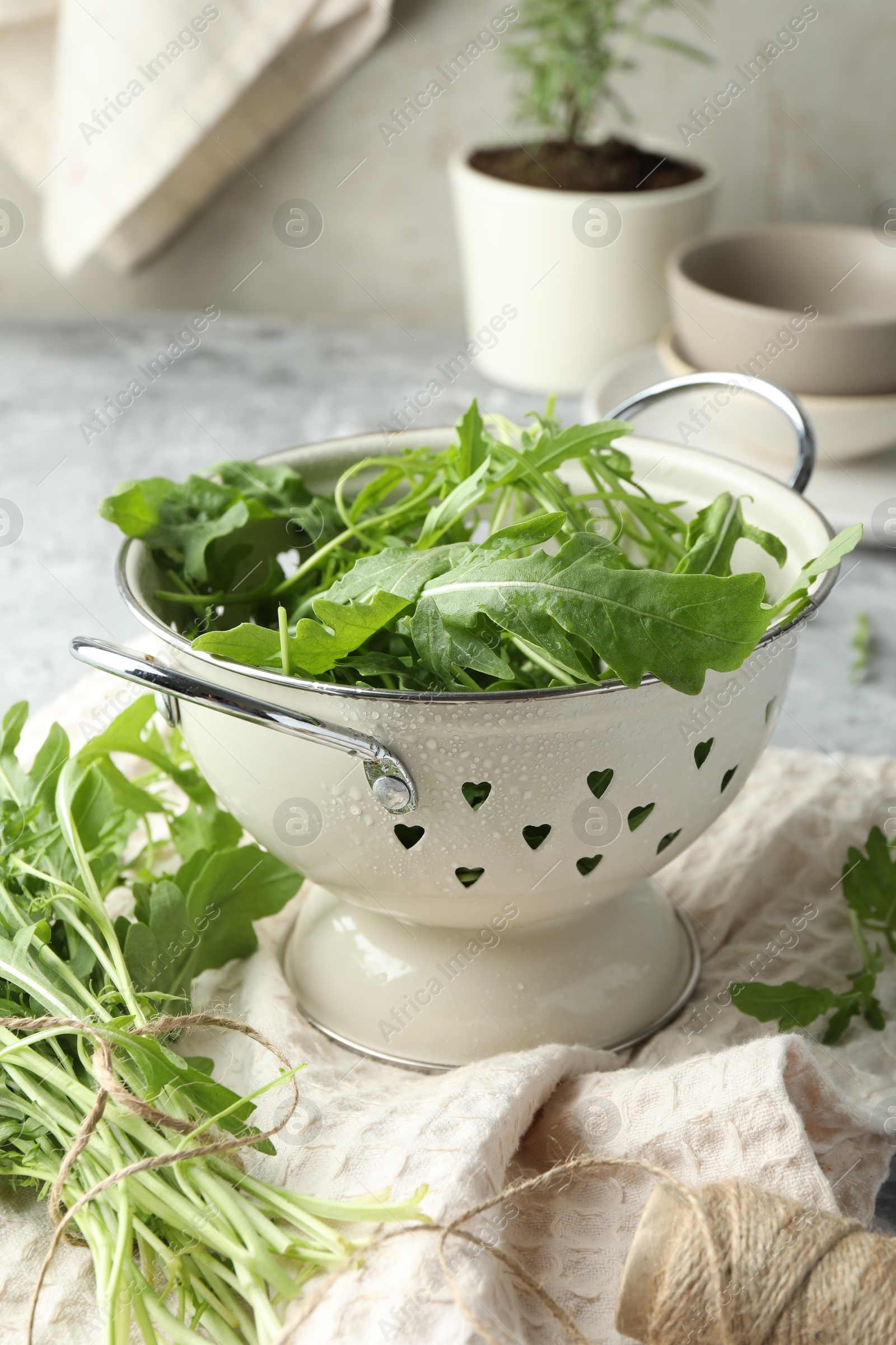 Photo of Fresh green arugula leaves in colander and spool of thread on table