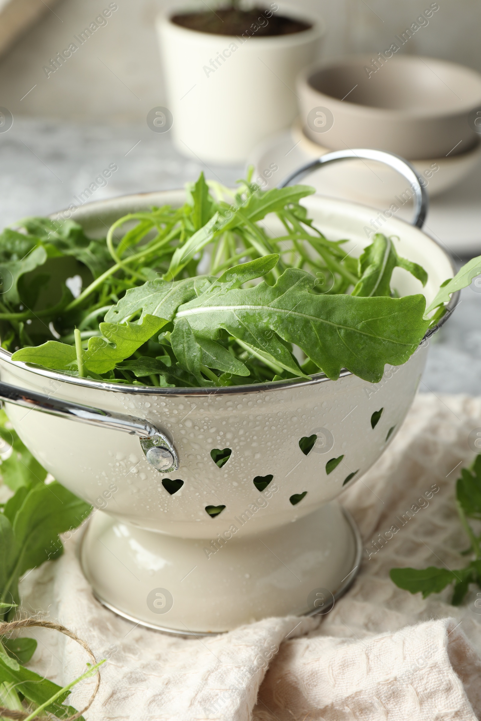 Photo of Fresh green arugula leaves in colander on table, closeup