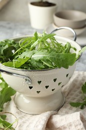 Photo of Fresh green arugula leaves in colander on table, closeup