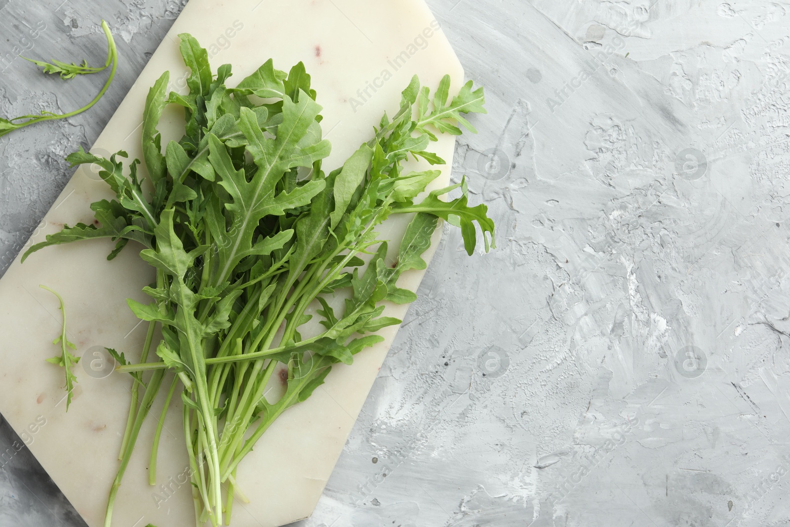 Photo of Fresh green arugula leaves on grey textured table, top view. Space for text