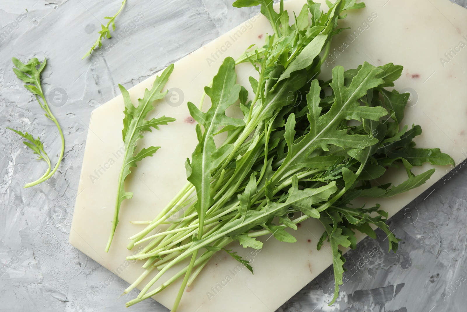 Photo of Fresh green arugula leaves on grey textured table, top view