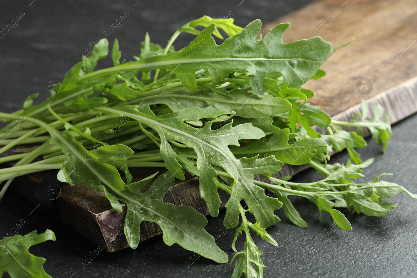 Photo of Fresh green arugula leaves on grey textured table, closeup