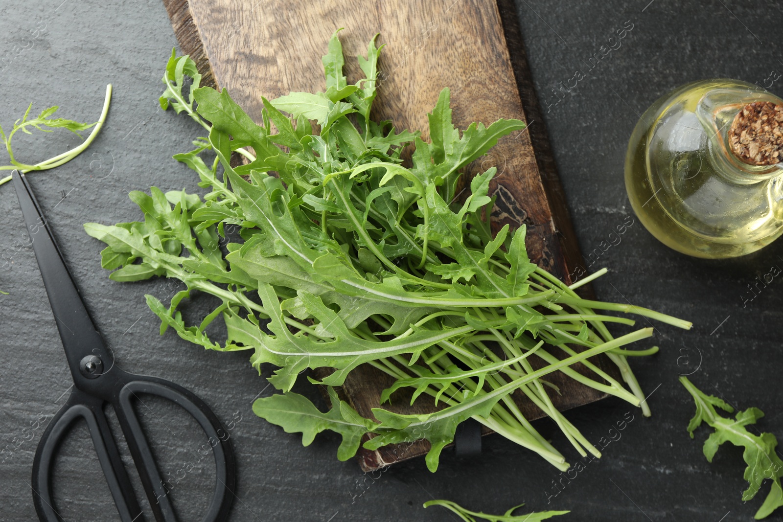 Photo of Fresh green arugula leaves, oil and scissors on grey textured table, flat lay