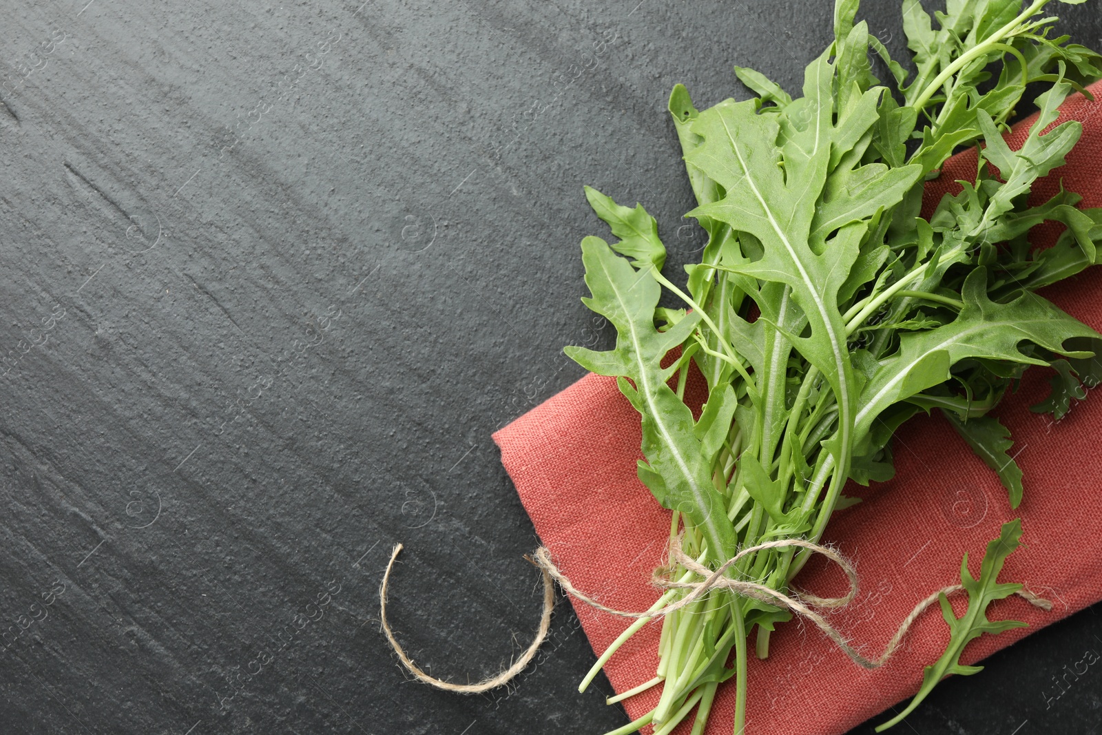 Photo of Bunch of fresh green arugula leaves on grey textured table, top view. Space for text