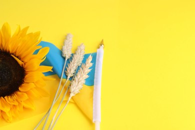 Photo of Ears of wheat, sunflower and Ukrainian national flag on yellow background, closeup. Space for text