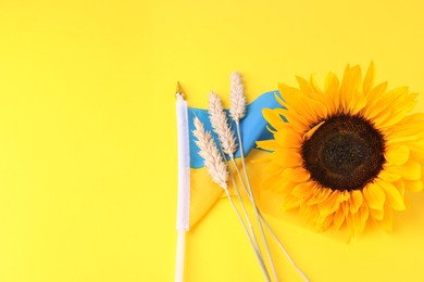 Photo of Ears of wheat, sunflower and Ukrainian national flag on yellow background. Space for text