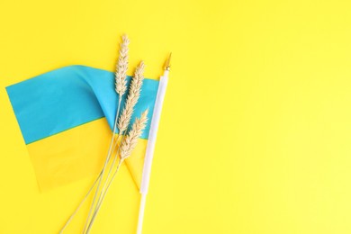 Photo of Ears of wheat and Ukrainian national flag on yellow background, flat lay. Space for text