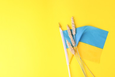 Ears of wheat and Ukrainian national flag on yellow background, flat lay. Space for text