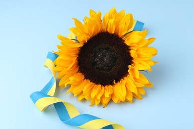 Photo of Sunflower with ribbon in colors of Ukrainian national flag on light blue background