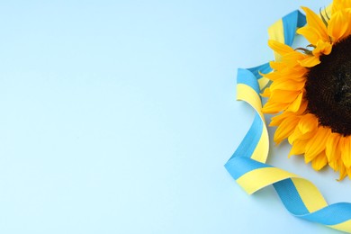 Sunflower with ribbon in colors of Ukrainian national flag on light blue background, space for text