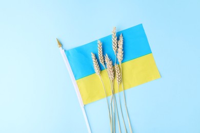 Photo of Ears of wheat and Ukrainian flag on light blue background, top view