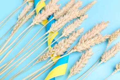 Photo of Ears of wheat with ribbon in colors of Ukrainian national flag on light blue background, closeup