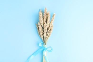 Ears of wheat with ribbons in colors of Ukrainian national flag on light blue background, top view