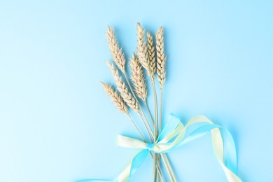 Ears of wheat with ribbons in colors of Ukrainian national flag on light blue background, top view