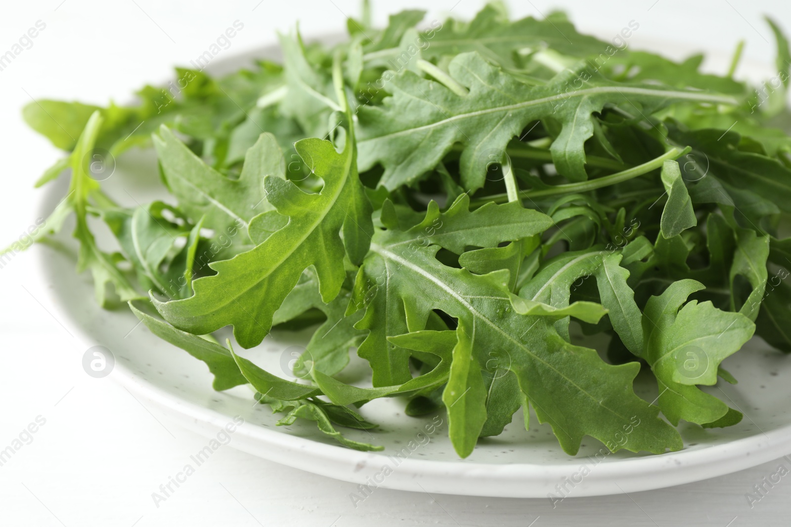 Photo of Fresh green arugula leaves on white table, closeup