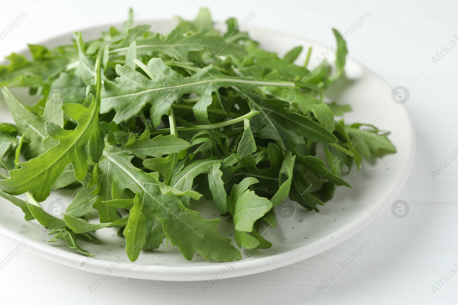 Photo of Fresh green arugula leaves on white table, closeup