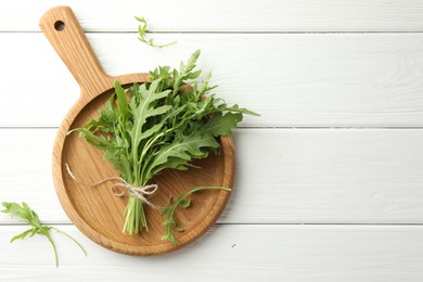 Photo of Bunch of fresh green arugula leaves on white wooden table, top view. Space for text