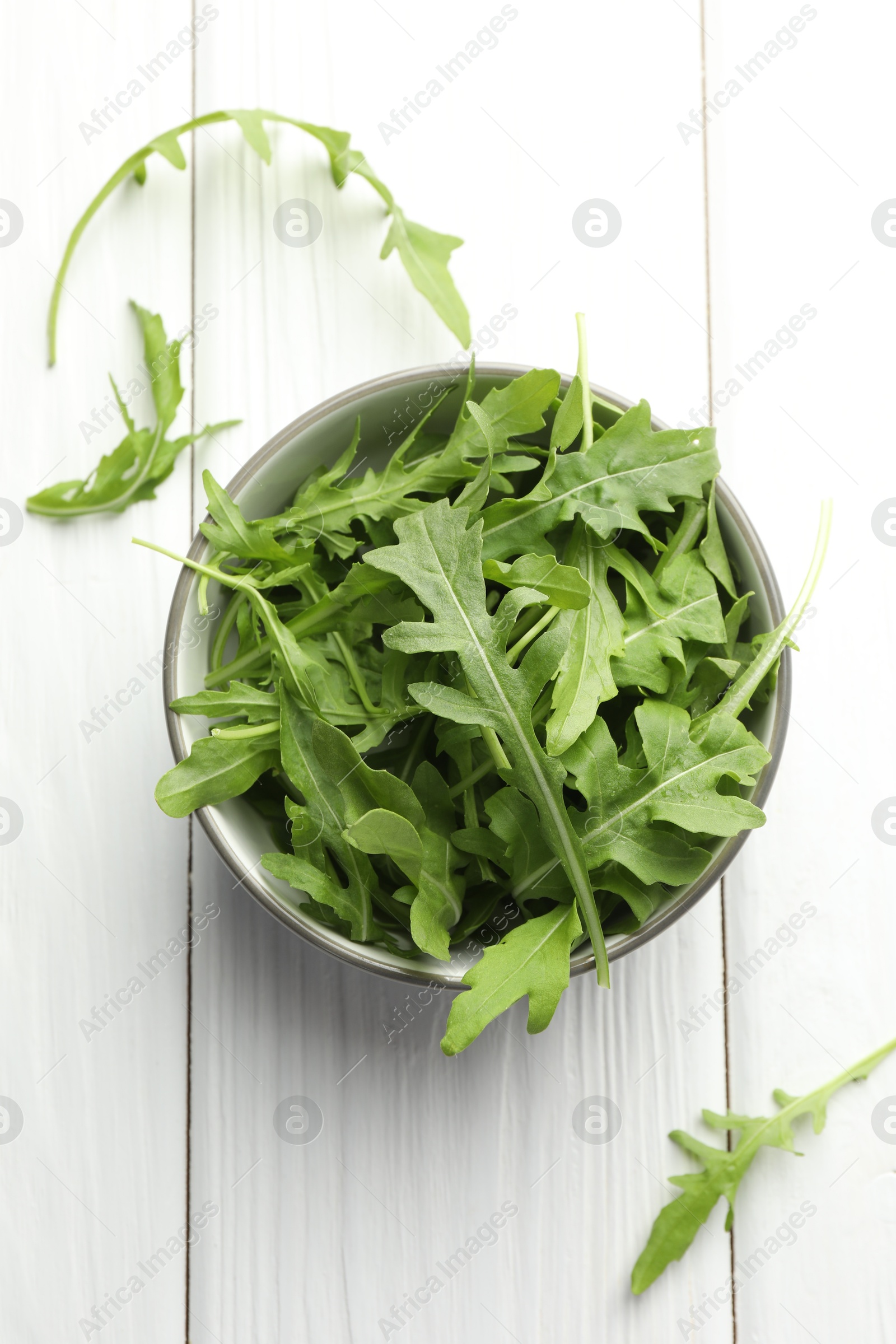 Photo of Fresh green arugula leaves in bowl on white wooden table, top view