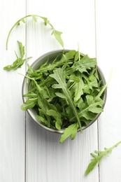 Photo of Fresh green arugula leaves in bowl on white wooden table, top view