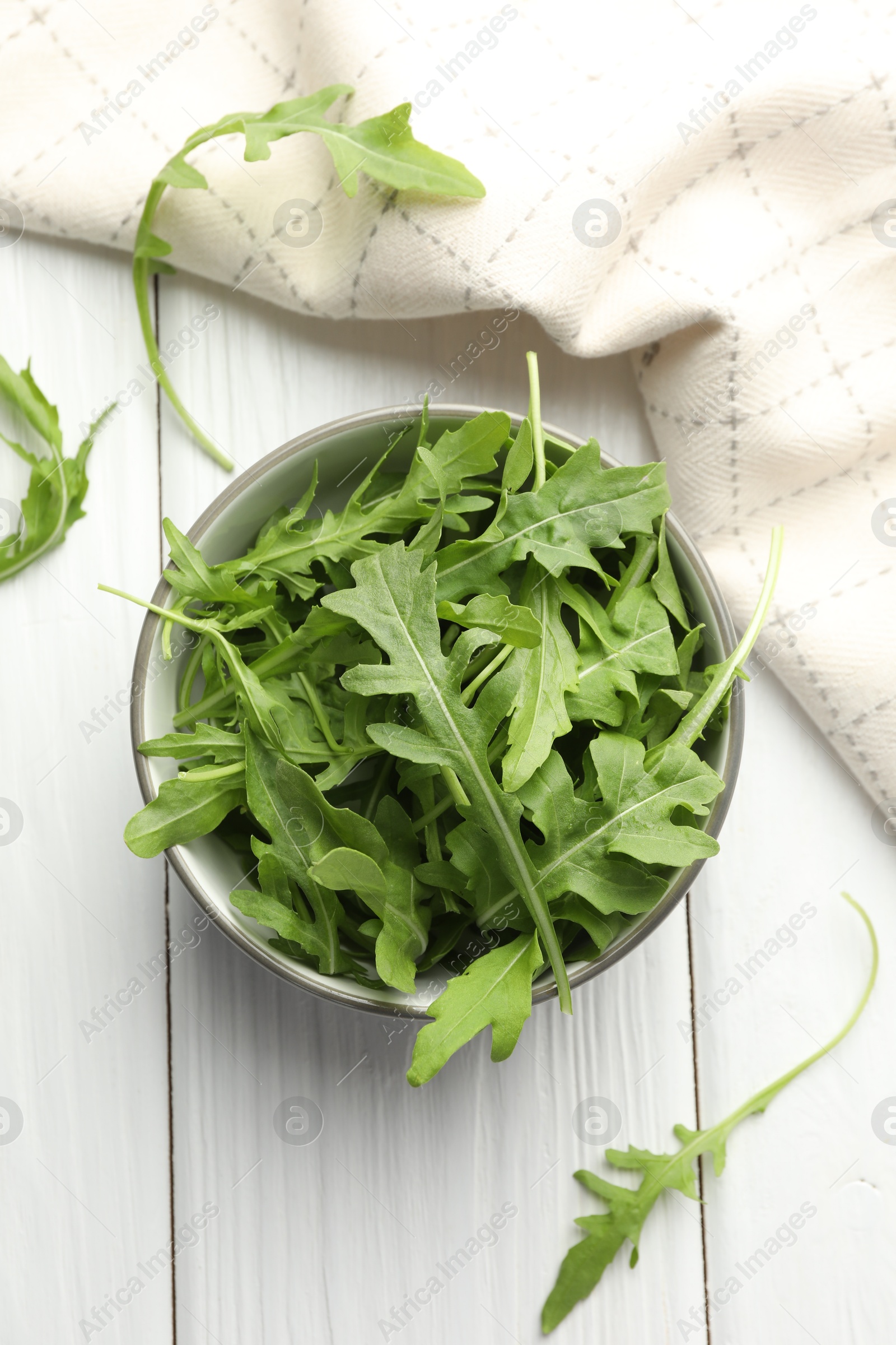 Photo of Fresh green arugula leaves in bowl on white wooden table, top view