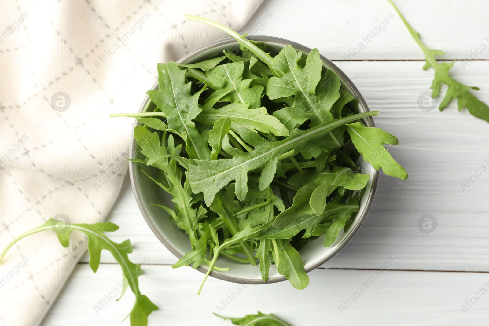 Photo of Fresh green arugula leaves in bowl on white wooden table, top view