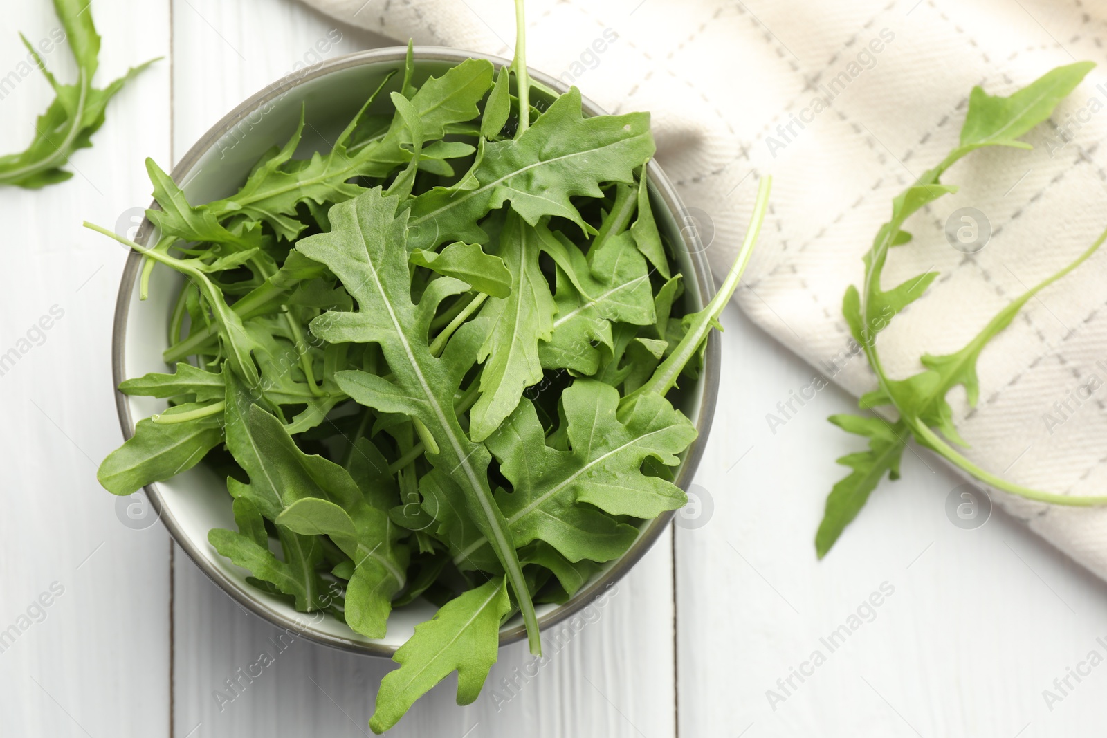 Photo of Fresh green arugula leaves in bowl on white wooden table, top view