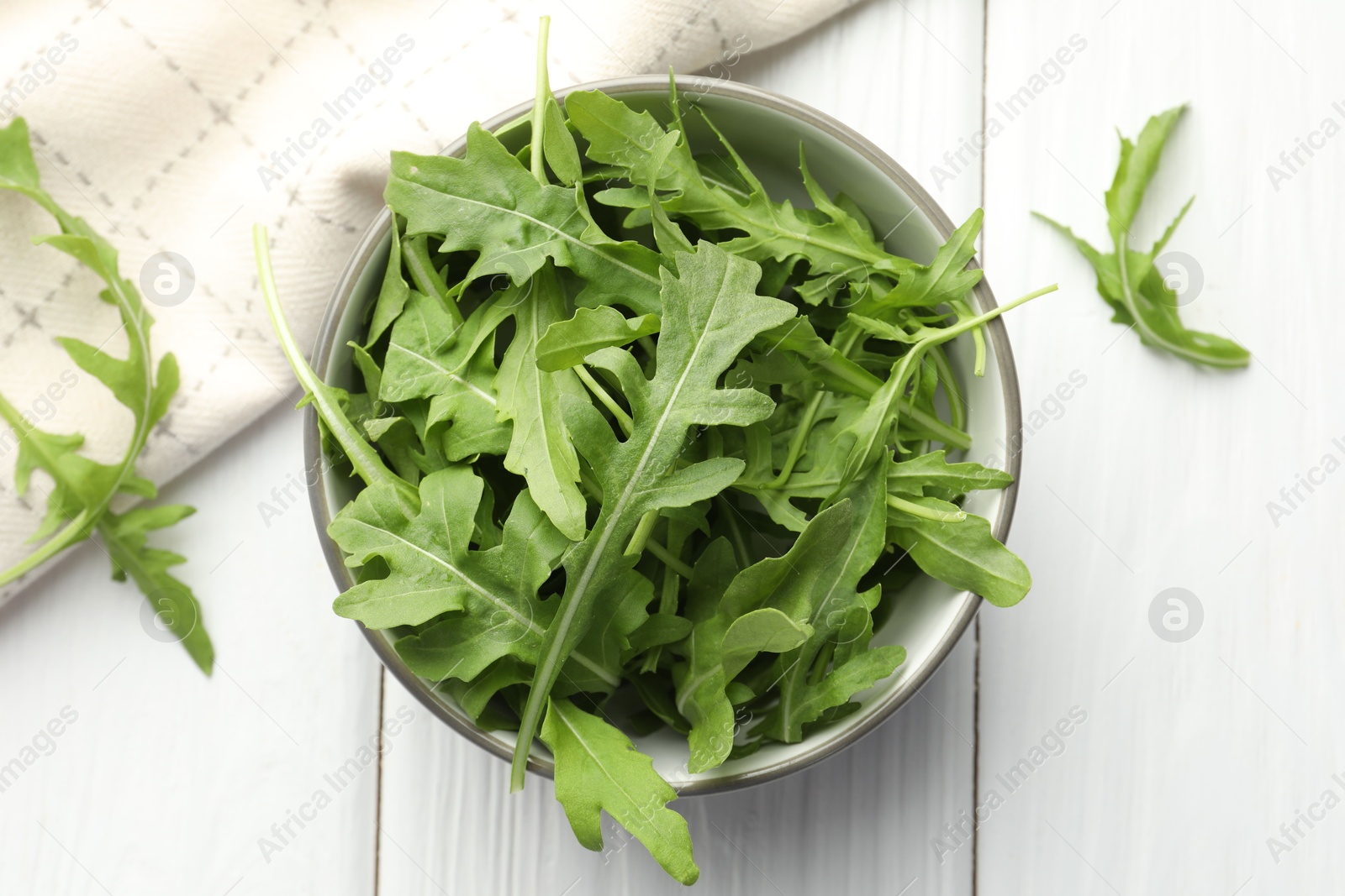 Photo of Fresh green arugula leaves in bowl on white wooden table, top view