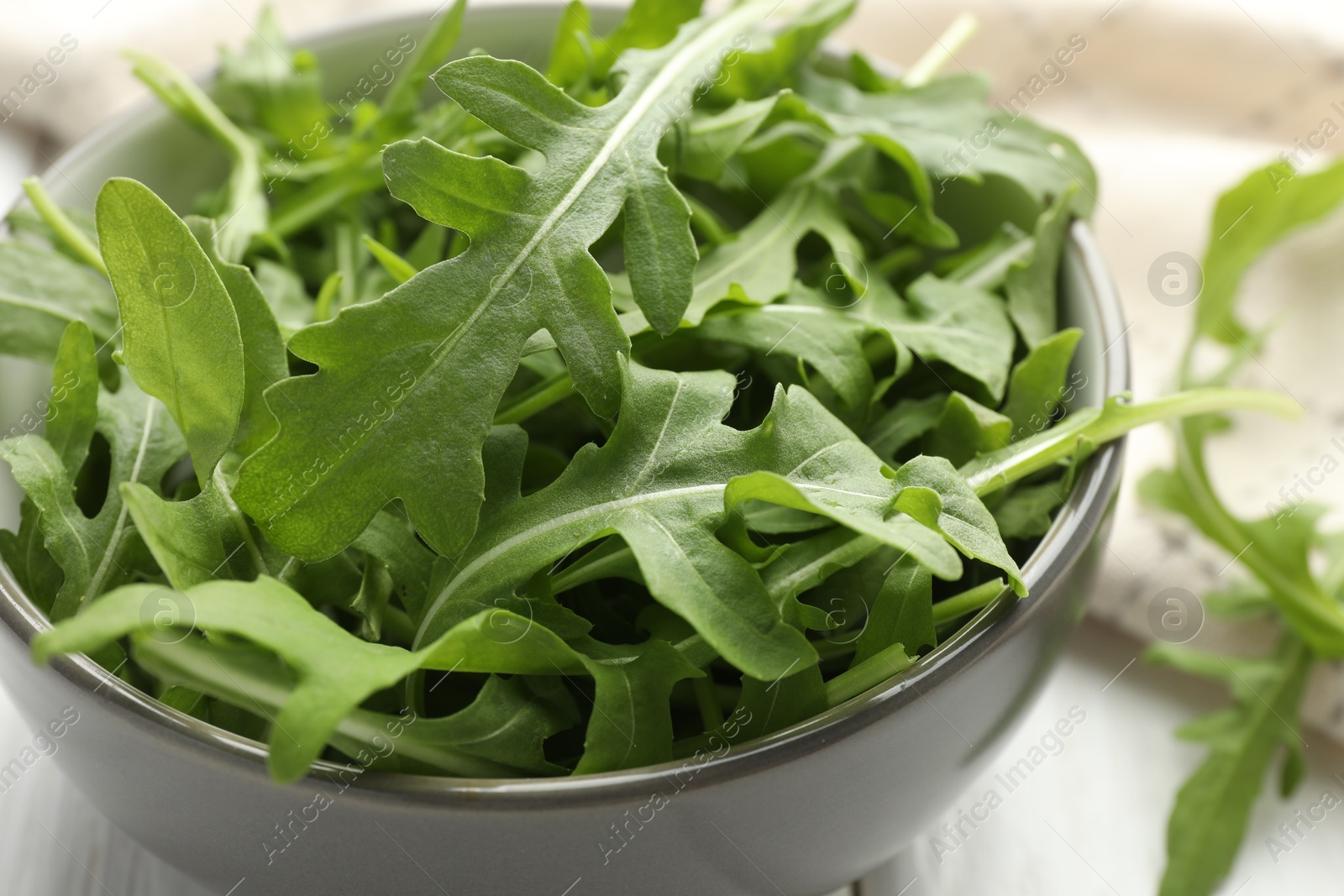 Photo of Fresh green arugula leaves in bowl on white table, closeup