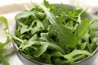 Photo of Fresh green arugula leaves in bowl on white table, closeup