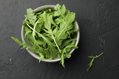 Photo of Fresh green arugula leaves in bowl on grey textured table, top view