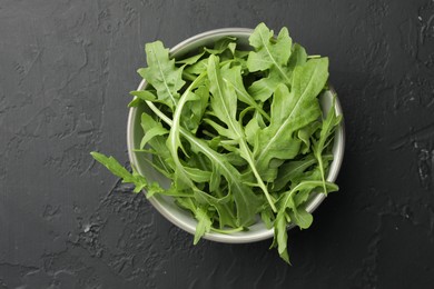 Photo of Fresh green arugula leaves in bowl on grey textured table, top view