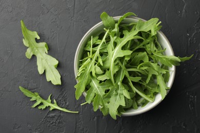 Photo of Fresh green arugula leaves in bowl on grey textured table, top view