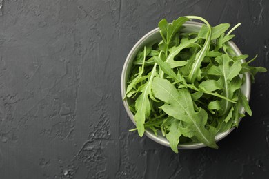 Photo of Fresh green arugula leaves in bowl on grey textured table, top view. Space for text