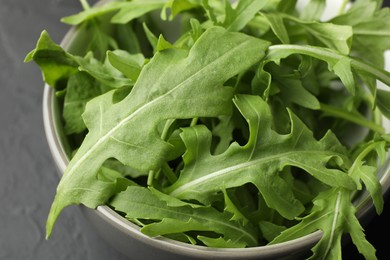 Photo of Fresh green arugula leaves in bowl on grey table, closeup