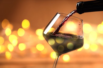 Pouring tasty wine into glass against blurred lights, closeup. Bokeh effect