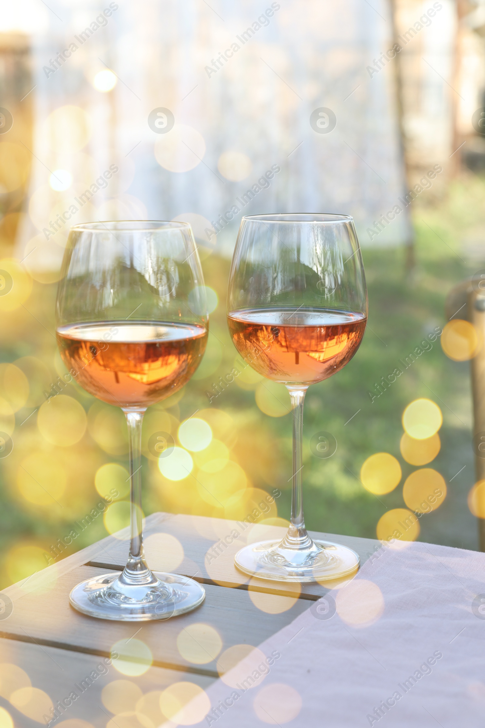 Image of Rose wine in glasses on wooden table in garden. Bokeh effect