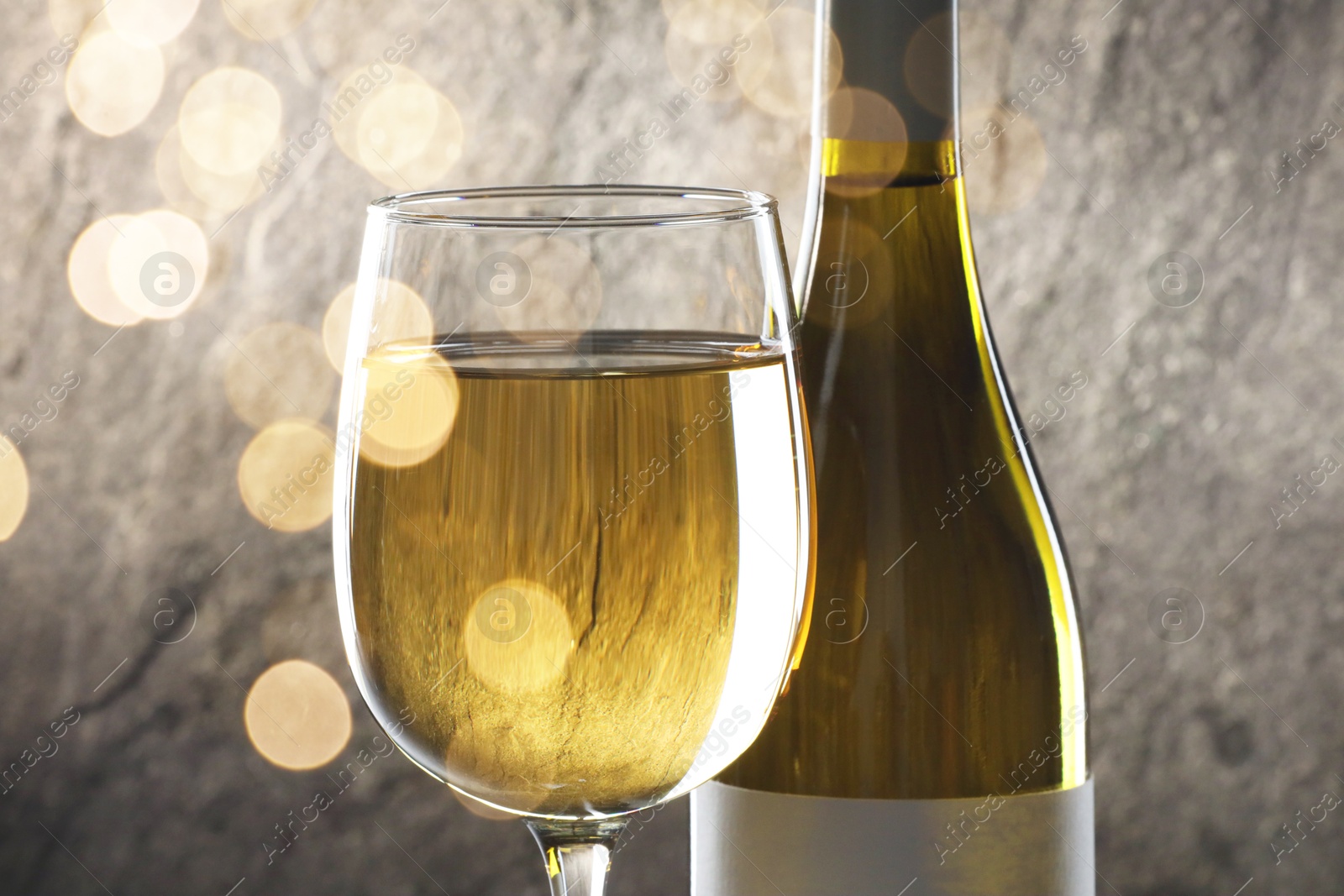 Image of White wine in glass and bottle against grey background. Bokeh effect